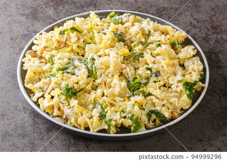 Delicious fragrant Mafalda pasta with wild arugula, crispy pistachios, parmesan cheese and lemon zest close-up on a plate. horizontal Delicious fragrant Mafalda pasta with wild arugula, crispy pistachios, parmesan cheese and lemon zest close-up on a plate. horizontal 94999296
