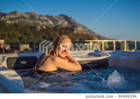 Portrait of young carefree happy smiling woman relaxing at hot tub during enjoying happy traveling moment vacation life against the background of green big mountains 94999394