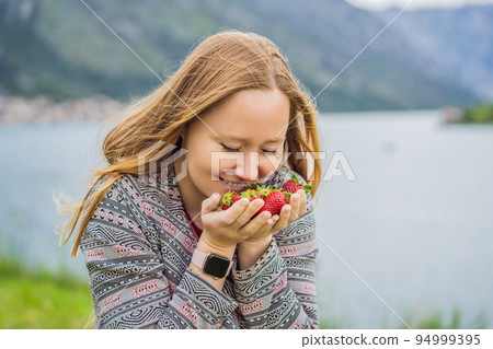 Young attractive woman eating a strawberry, outdoors Young attractive woman eating a strawberry, outdoors 94999395