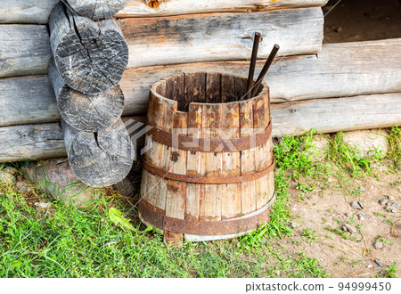 Vintage wooden barrel with rusty metal hoops near wooden house 94999450
