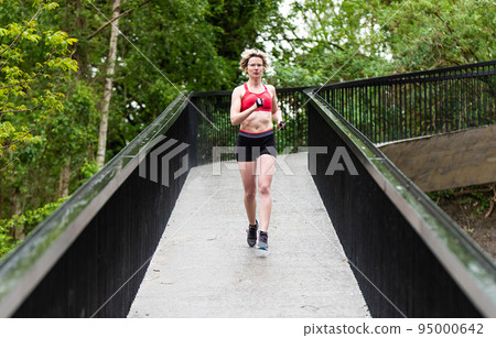 Healthy thirty year old woman running on a pedestrian bridge outdoors Healthy thirty year old woman running on a pedestrian bridge outdoors 95000642