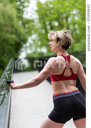 Attractive athlete woman standing on a pedestrian bridge in the woods Attractive athlete woman standing on a pedestrian bridge in the woods 95000645