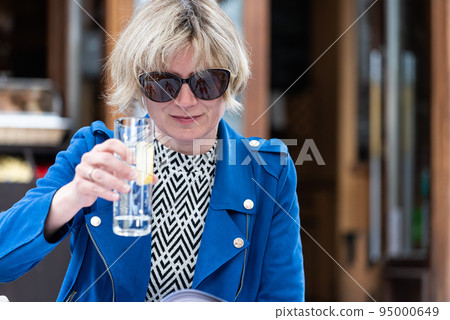 Attractive thirty year old woman with sunglasses drinking a glass of water on a terrace Attractive thirty year old woman with sunglasses drinking a glass of water on a terrace 95000649
