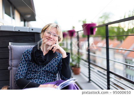 Portrait of an attractive thirty year old woman sitting on a terrace, reading 95000650