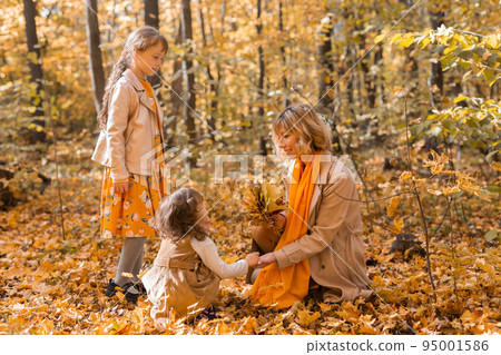 Young mother with her little daughters in an autumn park. Fall season, parenting and children concept. 95001586