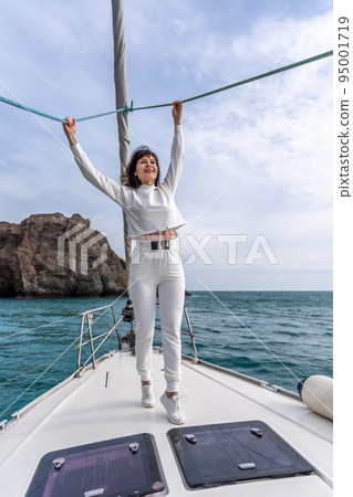 Woman standing on the nose of the yacht at a sunny summer day, breeze developing hair, beautiful sea on background Woman standing on the nose of the yacht at a sunny summer day, breeze developing hair, beautiful sea on background 95001719