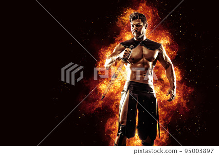 Sportive man in leather warrior costume with sword, fire on background 95003897