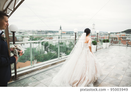 Stylish couple of happy newlyweds. Bride running from groom in the park on their wedding day with bouquet 95003949