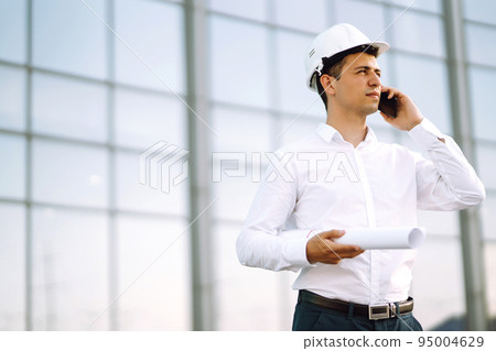 Young worker in a helmet and with a phone at a work object. Business, building 95004629