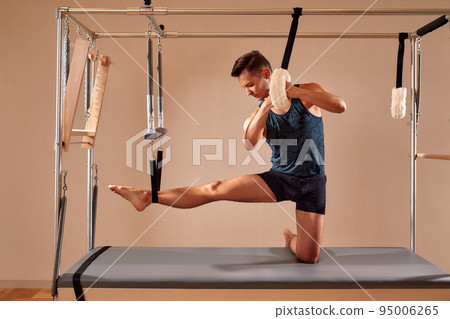 Fit man doing a lunge stretch yoga pilates exercise to strengthen and tone his muscles using a reformer in gym. Health and fitness concept 95006265