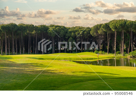 Sunset or dawn over a golf course overlooking a body of water and even green grass 95008546