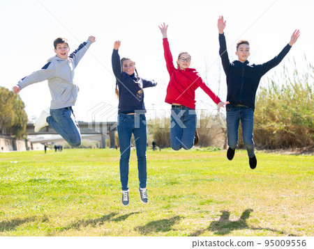 Cheerful teenages jumping in spring city park 95009556