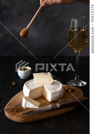 Homemade camembert on a wooden board is watered with honey, there is a glass of wine on the background. Vertical photo. 95013174
