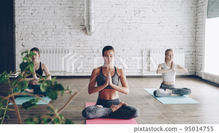Young attractive spiritual girls are doing relaxation breating exercises in yoga studio. Relaxing self-development energy concept. 95014755