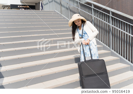 Young woman pulling suitcase up stairs Young woman pulling suitcase up stairs 95016419