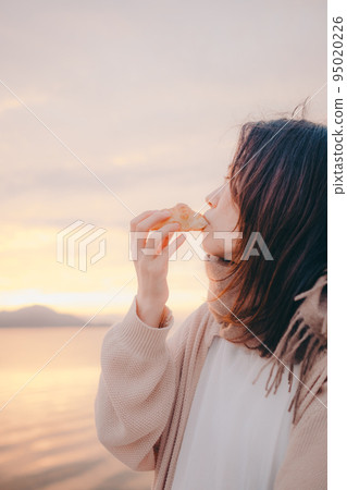 Photo of a woman eating bread with a beautiful sunrise 95020226
