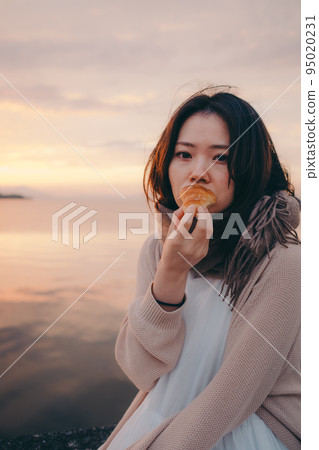 Photo of a woman eating bread with a beautiful sunrise 95020231