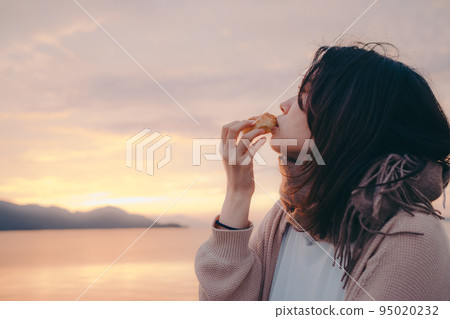 Photo of a woman eating bread with a beautiful sunrise 95020232