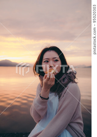 Photo of a woman eating bread with a beautiful sunrise Photo of a woman eating bread with a beautiful sunrise 95020303