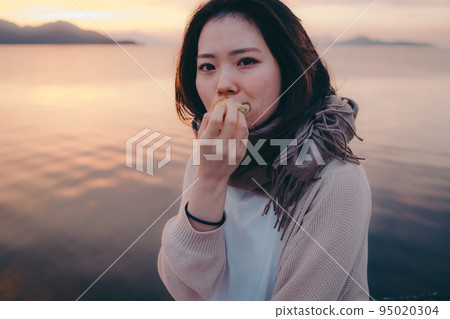 一個女人在美麗的日出中吃麵包的照片 95020304