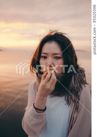 一個女人在美麗的日出中吃麵包的照片 95020306