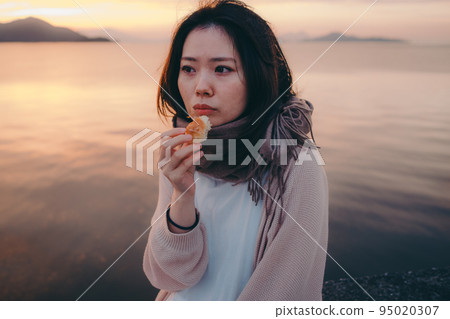 一個女人在美麗的日出中吃麵包的照片 95020307