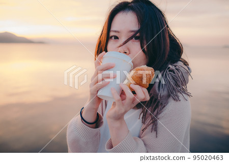 Photo of a woman eating bread with a beautiful sunrise 95020463