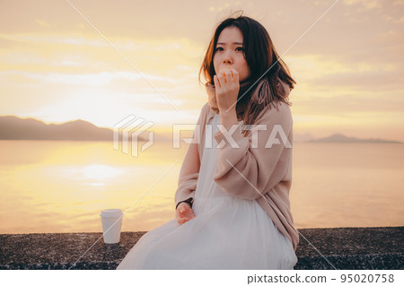 一個女人在美麗的日出中吃麵包的照片 95020758