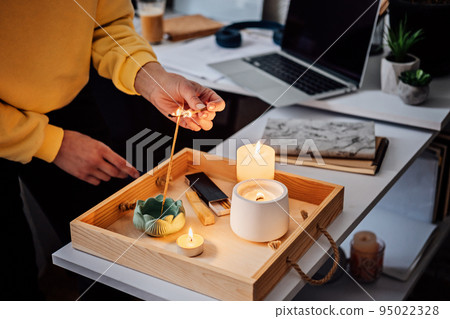 Meditation, relaxation after work. Woman getting ready meditating and lights up indian incense stick and candles. Woman hands with Smoke indian incense stick, burning candles on the table at home Meditation, relaxation after work. Woman getting ready meditating and lights up indian incense stick and candles. Woman hands with Smoke indian incense stick, burning candles on the table at home 95022328