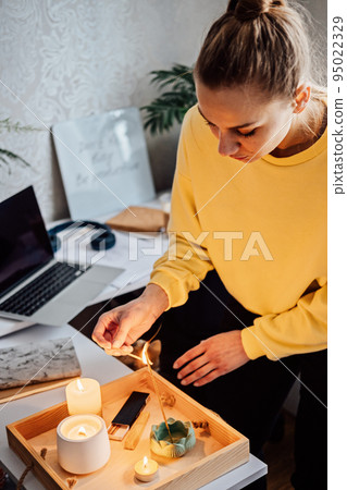 Meditation, relaxation after work. Woman getting ready meditating and lights up indian incense stick and candles. Woman hands with Smoke indian incense stick, burning candles on the table at home Meditation, relaxation after work. Woman getting ready meditating and lights up indian incense stick and candles. Woman hands with Smoke indian incense stick, burning candles on the table at home 95022329