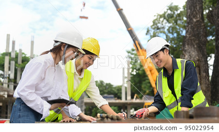 Engineer team discussing industrial building design project at construction site against mobile crane on background 95022954