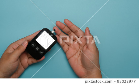 From above view of woman with glucometer checking blood sugar level on blue background. Diabetes, health care and people concept From above view of woman with glucometer checking blood sugar level on blue background. Diabetes, health care and people concept 95022977