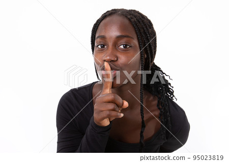 Portrait of happy young woman standing with finger on lips 95023819