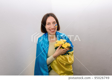 Young girl with blue and yellow flowers and the National Flag of Ukraine. Flag is painted on woman's cheek. Stop war. Copy space. Young girl with blue and yellow flowers and the National Flag of Ukraine. Flag is painted on woman's cheek. Stop war. Copy space. 95026749