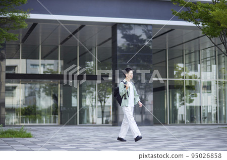A young male student leaning against the wall of a school building inside the campus. A young male student leaning against the wall of a school building inside the campus. 95026858