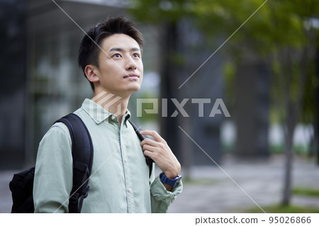 A young male student leaning against the wall of the school building in front of it. A young male student leaning against the wall of the school building in front of it. 95026866
