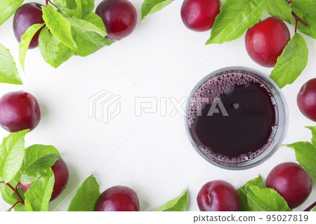 Fresh plums kampot juice in a glass on a background of plums with leaves on a white concrete background. Autumn summer drinks. Canning or harvesting. Copy space. 95027819