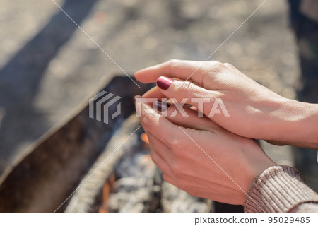 barbecue in the Park. a girl warms his hands by the fire, natural wood smolder in the grill, the coals are covered with ash 95029485