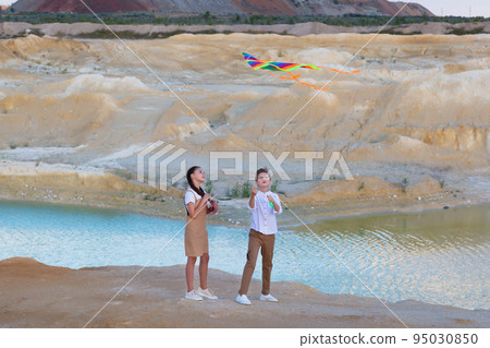 A boy and a girl launch a bright kite into the sky in the mountains near the river 95030850