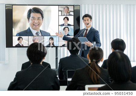 A business seminar with an external lecturer and a man moderating on a large monitor A business seminar with an external lecturer and a man moderating on a large monitor 95031450