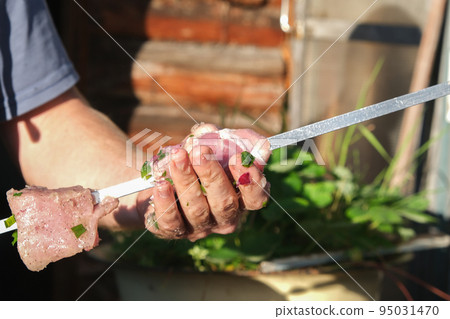 A man strands pickled meat on a skewer. A man puts A man strands pickled meat on a skewer. A man puts 95031470