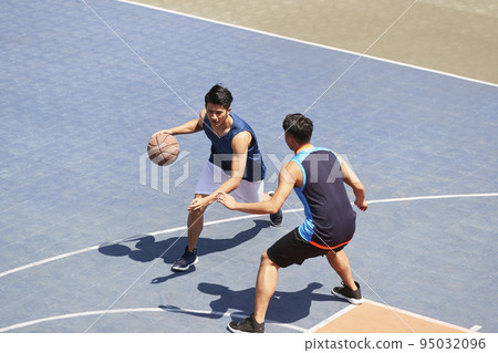 two young asian basketball players playing one on one on outdoor court 95032096