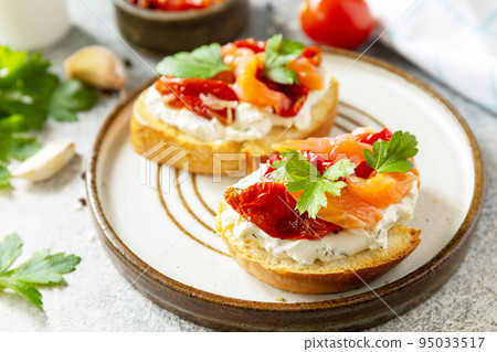 Open sandwiches or bruschetta with salted salmon, cheese and sun dried tomato on a stone table. Healthy food, seafood. 95033517