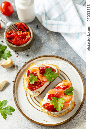 Open sandwiches or bruschetta with salted salmon, cheese and sun dried tomato on a stone table. Healthy food, seafood. 95033518