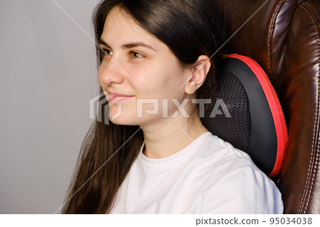A woman sits in a chair with a massage pillow and does a neck massage. A woman sits in a chair with a massage pillow and does a neck massage. 95034038