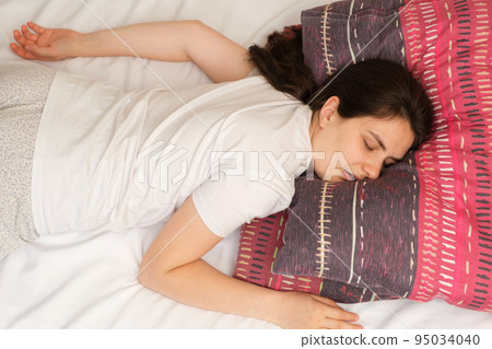 A woman lies on her stomach on a high pillow, opening her mouth, snoring, view from above. 95034040