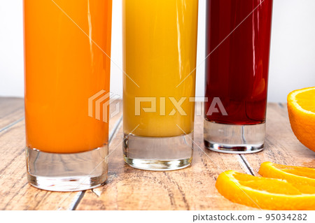 Three different fruit juices in glasses and fruits on a wooden background. Healthy nutrition for children and adults. Orange, cherry and tropical juice. Three different fruit juices in glasses and fruits on a wooden background. Healthy nutrition for children and adults. Orange, cherry and tropical juice. 95034282