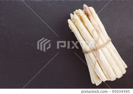 Bunch of fresh raw white asparagus spears on black background. Healthy greens, vegan food and ingredients for cooking concept. Closeup, copy space. 95034395