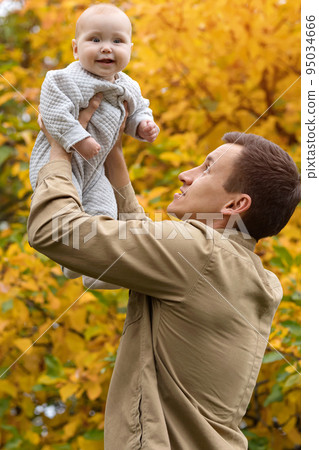 Father holds laughing baby high up against yellow trees 95034666