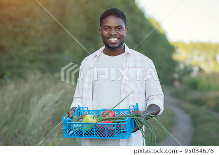 African American man walks with farm harvest in box by trees African American man walks with farm harvest in box by trees 95034676